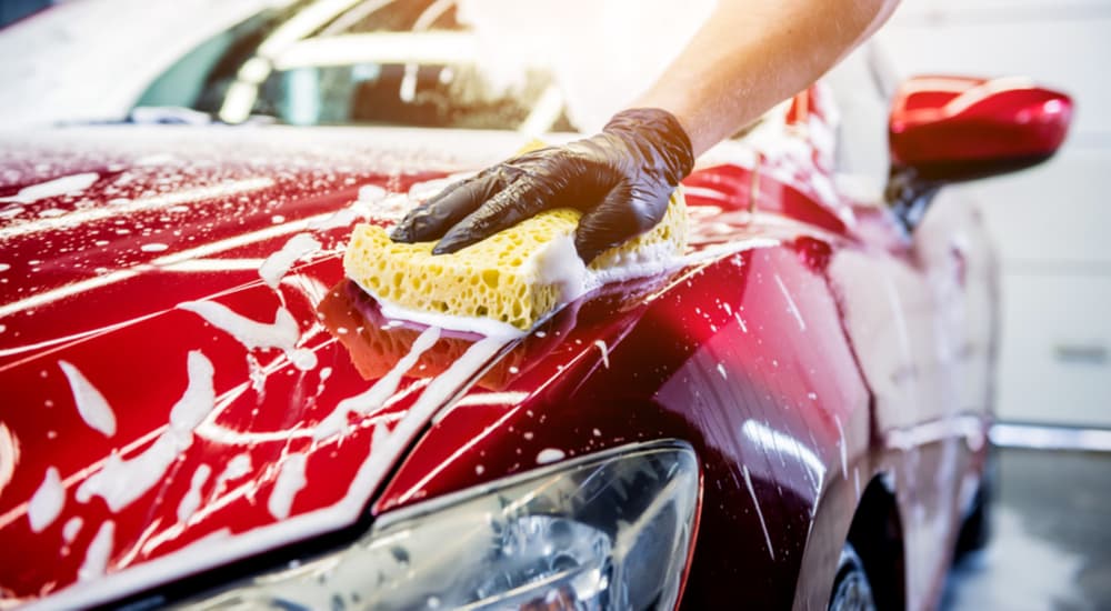 Person using a sponge to clean a red car