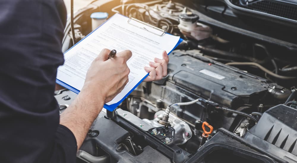 A mechanic holding a clipboard inspecting a vehicle